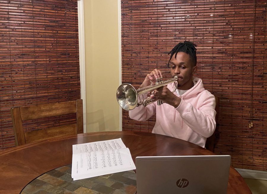 Adam Brooks (12) plays his trumpet, sheet music and laptop at hand. Restrictive virtual policies and snarky trumpet jokes alike haven’t stopped students from making music. 