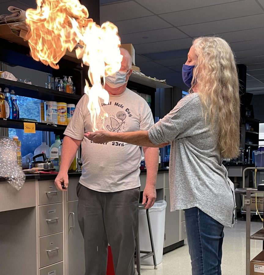 A retired physics and astronomy teacher holds out a large flame for a student audience. The flame was created by igniting methane bubbles.