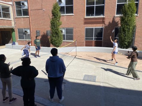 During a meeting after school, the badminton club starts a doubles match. Other members wait their turn and encourage the players.