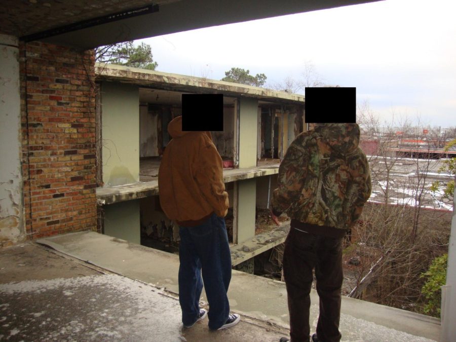 Two explorers gaze out over a dilapidated, unfinished building. Structures that are left behind to fall apart are enticing to many people who enjoy hobbies such as photography or graffiti.