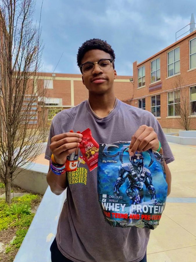 Football player and track runner Roman Laster (10) holds out his essential whey vanilla protein powder and favorite snacks: Gatorade Whey Protein Bar and Nature’s Garden Snack Mix.