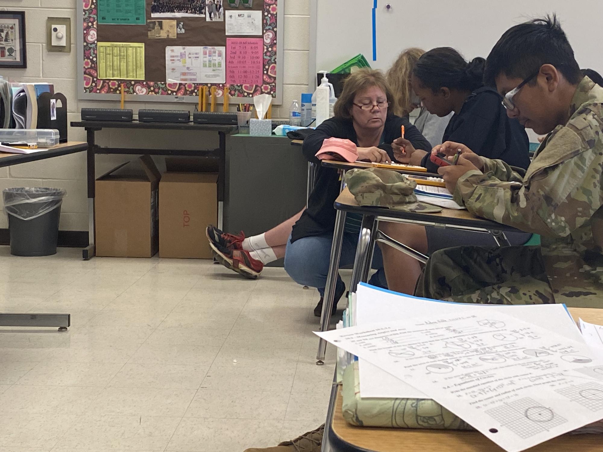 Teacher Poppy Underwood kneels to help students understand their work. She helped the students review circle formulas for their upcoming test.

