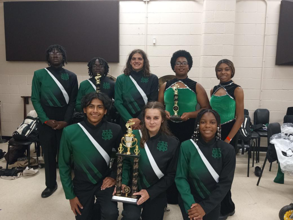 The+White+Station+High+School+marching+band%E2%80%99s+drum+majors%2C+color+guard+captains%2C+drumline+captain+and+co-captain+and+president+present+the+three+trophies+they+won+at+the+Arlington+Open+Invitational.+The+band+won+first+place+in+all+three+categories+within+their+division.