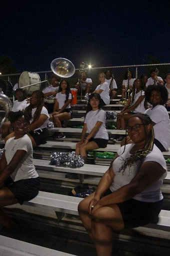 Color guard sits in formation before halftime. While the game is ongoing, they dance in unison to the band, and during halftime, they perform with flags in a field show.
